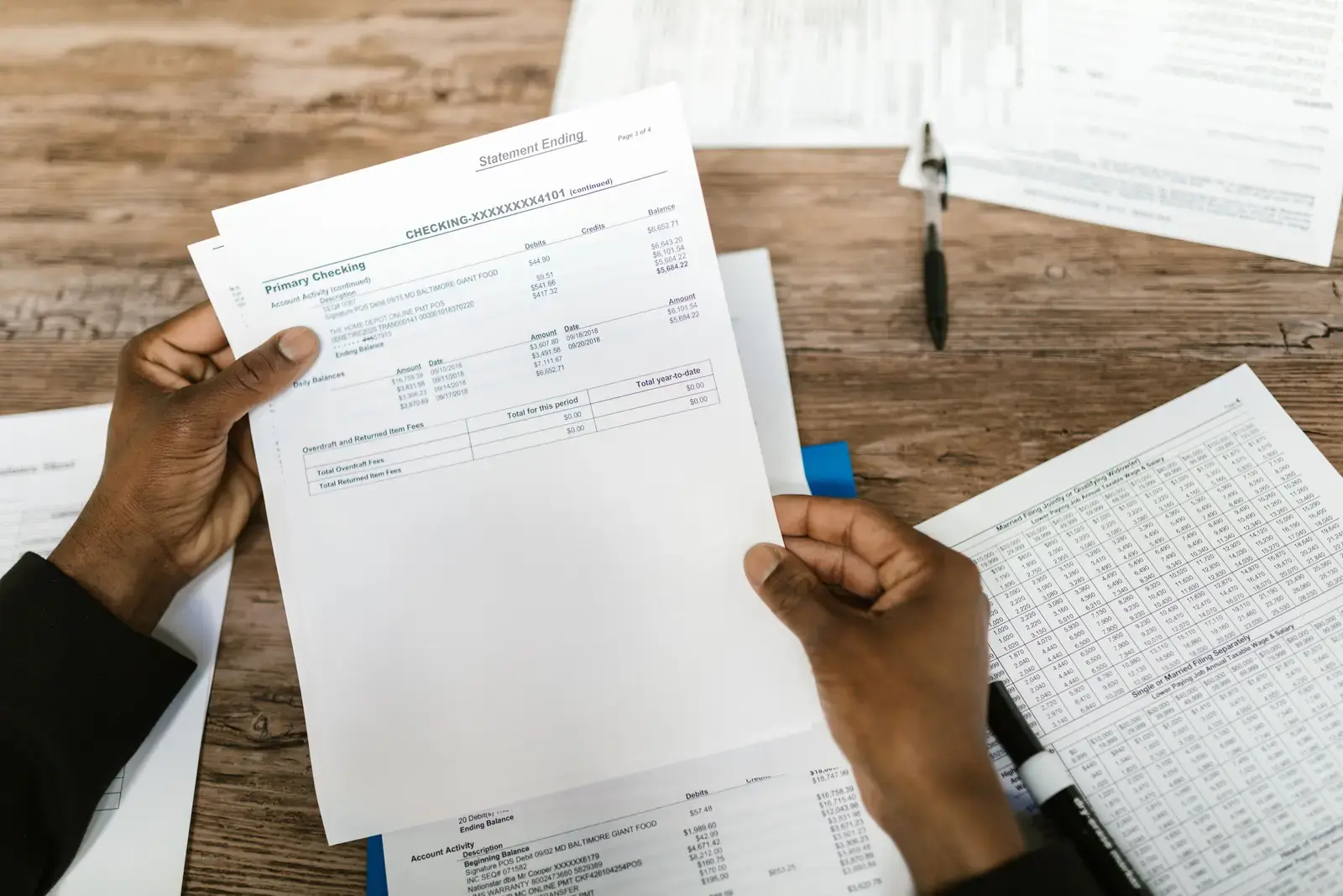 Hands holding printed bank statements over a desk of financial papers